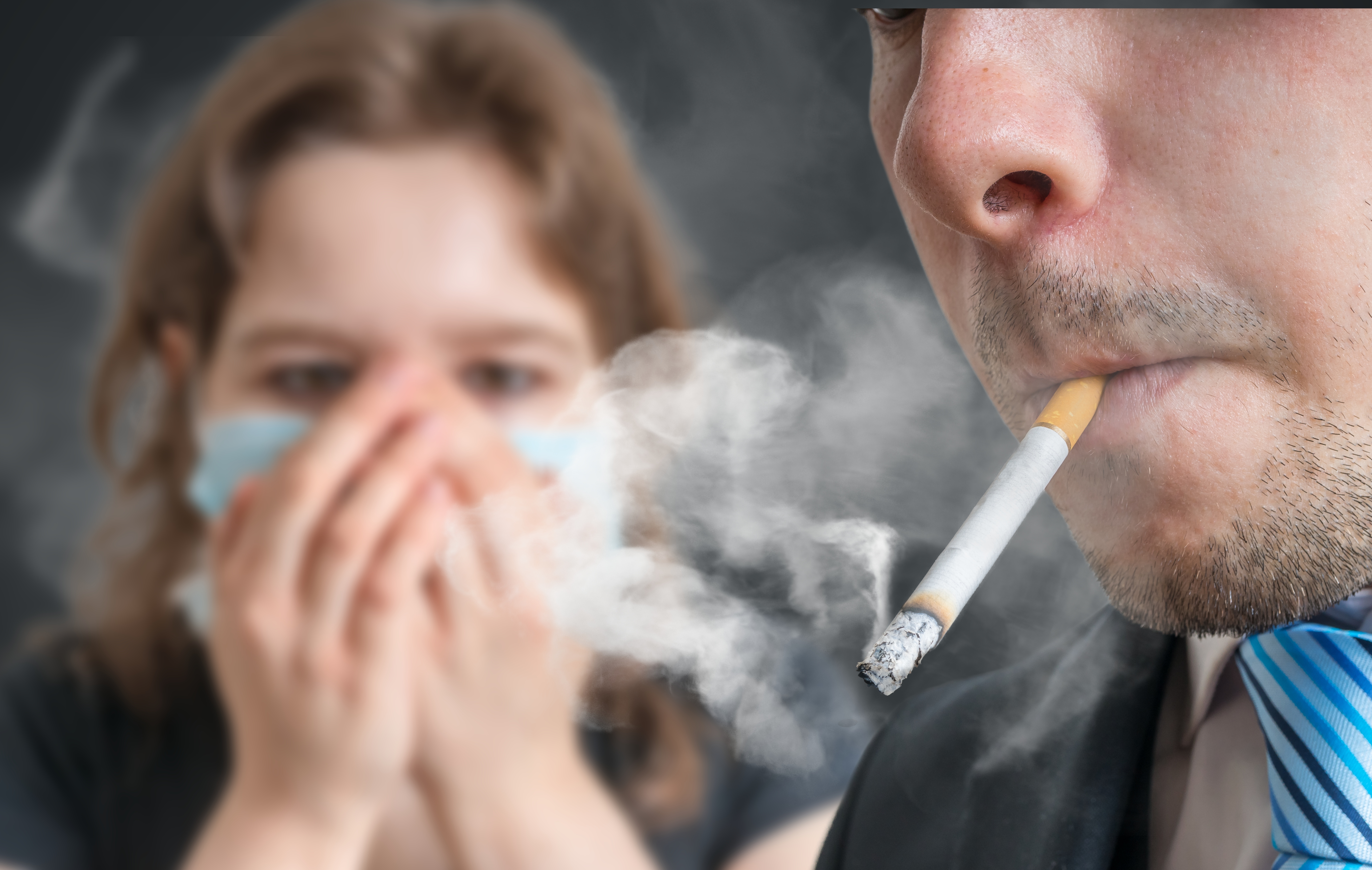 Person smoking a cigarette with another person in the background