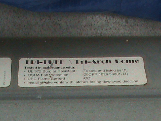 A metal placard reads Tri-Tuff Tri-Arch Dome, tested in accordance with UL 972 Burglar Resistant, OSHA fall protection, UBC Flame Spread, Tested and listed by UL, 29CFR 1926.500 B 4, CCI, and Install smoke vents with latches facing downwind direction.