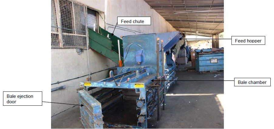 View showing chute leading from building into machine. A lower section of the machine protrudes out with a large gate on hinges that is open.