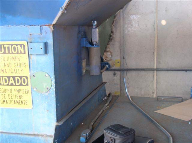 A metal cylinder sits in a holder welded to the side of a blue metal machine.