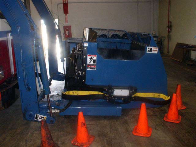 A side view of the collection bin shows the opening on top with a warning sign of the danger of being struck by the object.