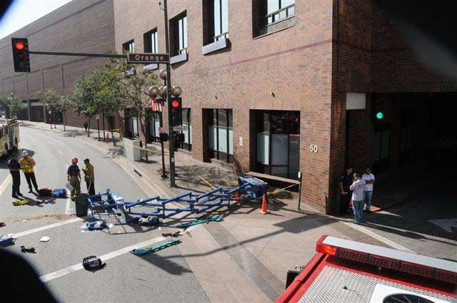 The fallen lift lies across a sidewalk and street beneath a window with a missing planter box underneath of it.
