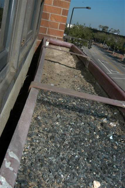 The outside of a planter is seen with a large gap between it and the window it is attached near.