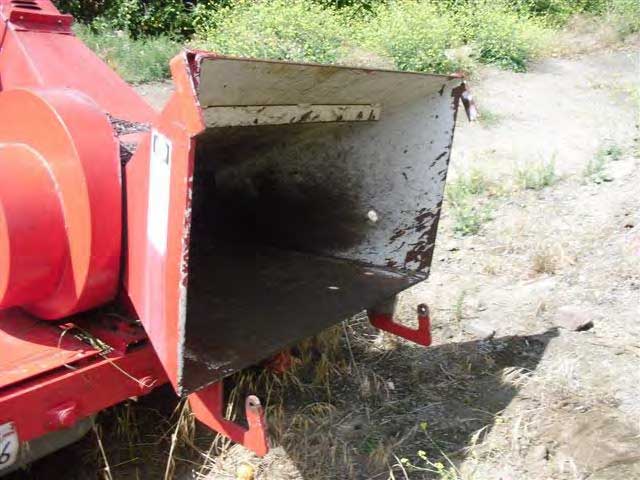 Two rusted hooks protrude from beneath the opening of the chipper and where the feed table should be installed.