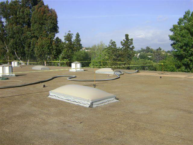 Rooftop showing skylights protruding from surface with hazard tape surrounding area where worker fell through broken skylight.