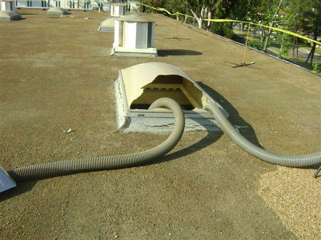 Close-up of broken skylight with jagged edges on rooftop with vacuum tubes running down into deep hole where worker fell through.