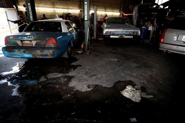 The vehicle involved in the incident is parked against a wall with a burned car next to it and a melted bucket on the ground that was used to pour gasoline into the car before the fire started.