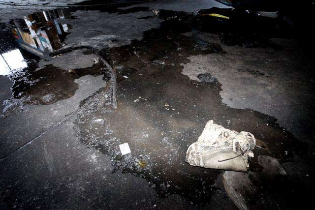 Remains of a bucket are on the floor of the garage. The bucket has been melted into a flat, lumpy mass.
