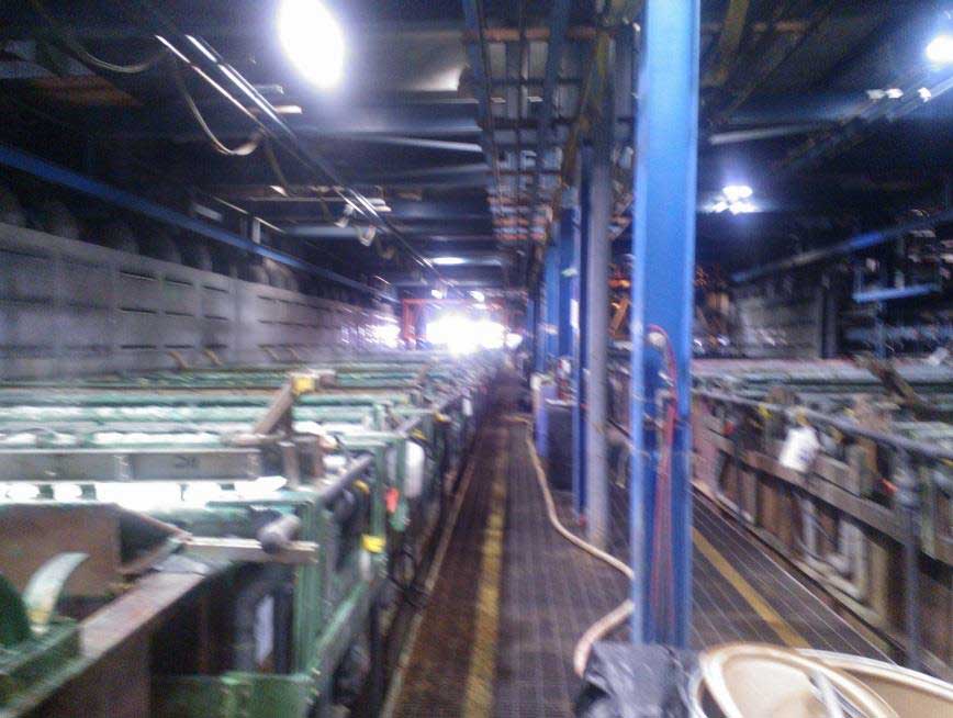 The chrome plating area of the business in a warehouse with narrow walkways along large tanks of liquid heavy metals.