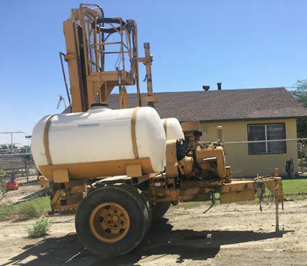 A spray rig atop a trailer with a raised bucket where a person stands.