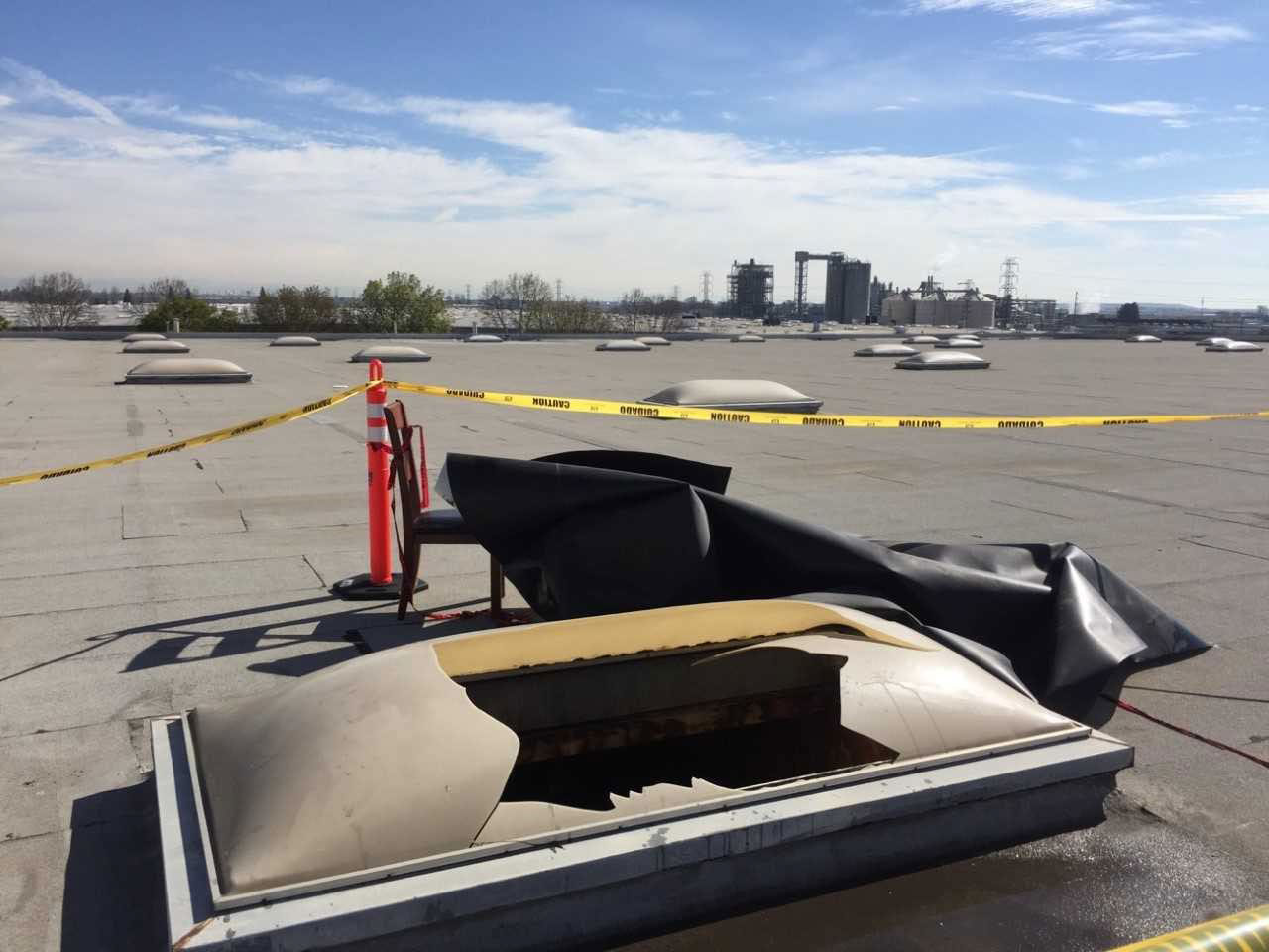 A broken skylight with jagged edges around a large hole is roped off from the rest of a rooftop with many skylights.
