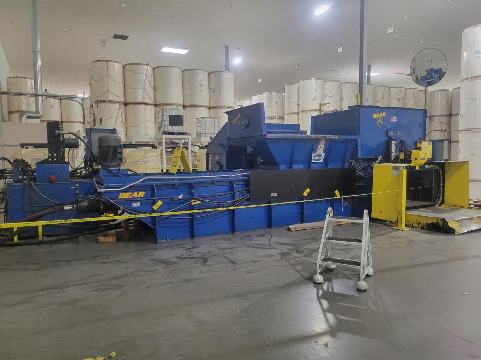 An industrial recycling baler with input hopper, indoor.
