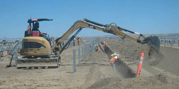 workers digging in dusty trench near a backhoe