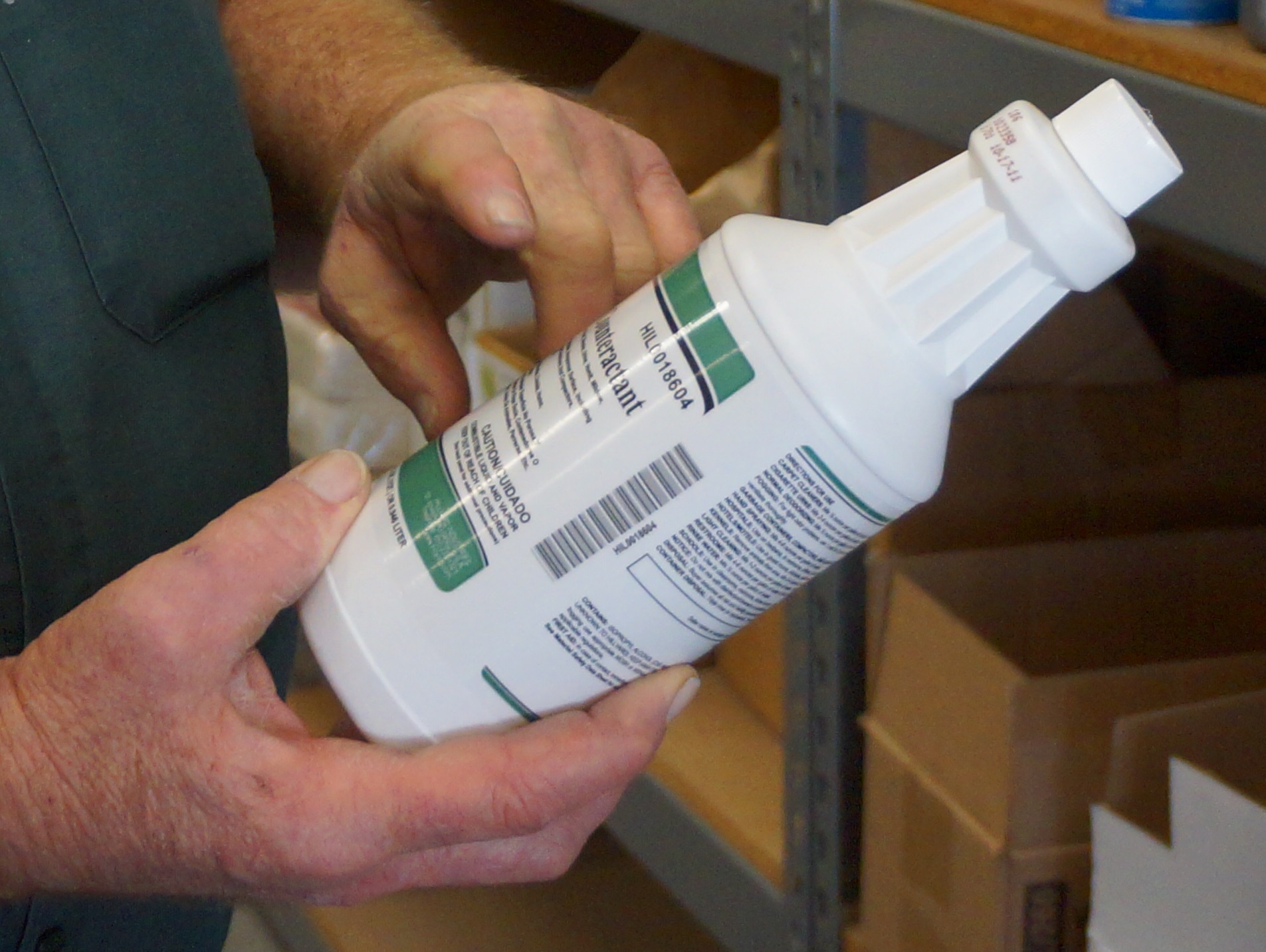 hands holding cleaning product bottle at an angle to read its ingredients
